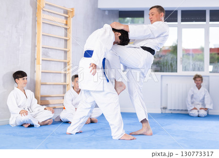 Karate sensei demonstrating fighting techniques to disciples during kumite with boy Karate sensei demonstrating fighting techniques to disciples during kumite with boy 130773317