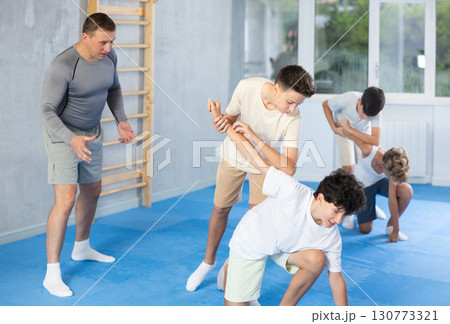 Diligent preteen student twisting his opponent's arm in sports hall Diligent preteen student twisting his opponent's arm in sports hall 130773321