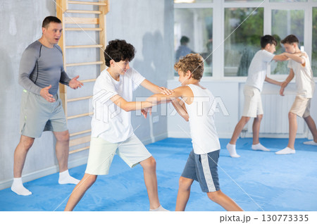 Positive kids in pair exercising self-defense movements during group class with male coach 130773335