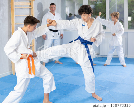 Teenage boys in kimonos practicing karate kicking techniques during sparring Teenage boys in kimonos practicing karate kicking techniques during sparring 130773339