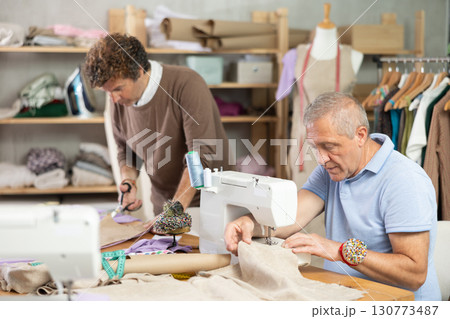 Mature man tailor at work, other man cut out paper dress pattern Mature man tailor at work, other man cut out paper dress pattern 130773487