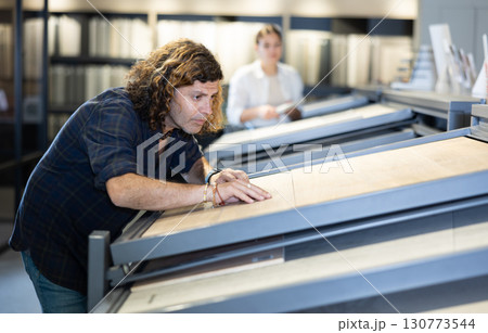 in hardware store,male buyer carefully examines laminate sample. Man chooses flooring material 130773544