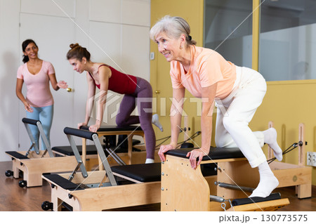 Female instructor helps women perform an exercise on a combined chair 130773575