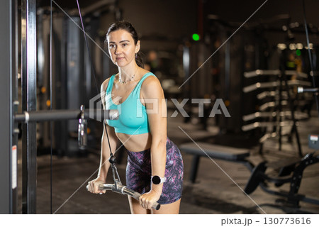 In gym, woman uses cable row machine to strengthen muscles. In gym, woman uses cable row machine to strengthen muscles. 130773616