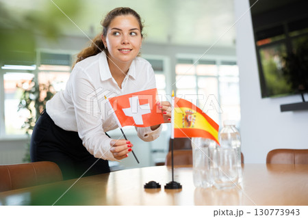 Young woman puts flags of Switzerland and Spain on table in office 130773943