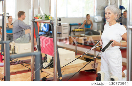 Elderly woman training her arms using straps Elderly woman training her arms using straps 130773944