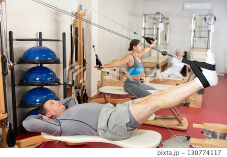Man is engaged in Pilates simulator with cable and ropes for stretching leg muscles Man is engaged in Pilates simulator with cable and ropes for stretching leg muscles 130774117