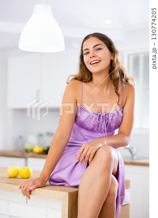 Portrait of attractive young woman sitting on kitchen table Portrait of attractive young woman sitting on kitchen table 130774205