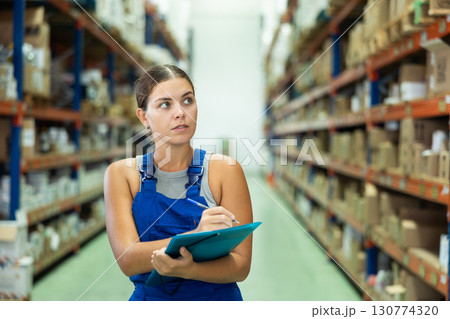 Focused saleswoman standing with papers and checking goods availability on shelves of building hypermarket 130774320