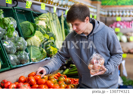 Young guy chooses tomatoes in vegetable shop 130774321
