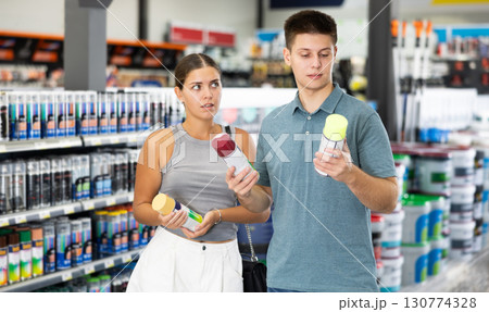 Young married couple chooses cans of aerosol paint in hardware store 130774328