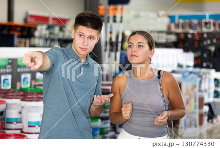 Young positive woman and man shopping in building store, man pointing to something Young positive woman and man shopping in building store, man pointing to something 130774330