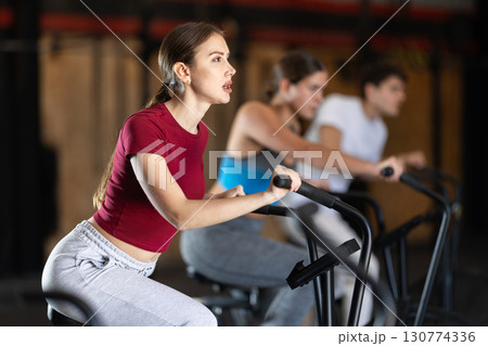 Focused girl works out with airbike during class at fitness club Focused girl works out with airbike during class at fitness club 130774336