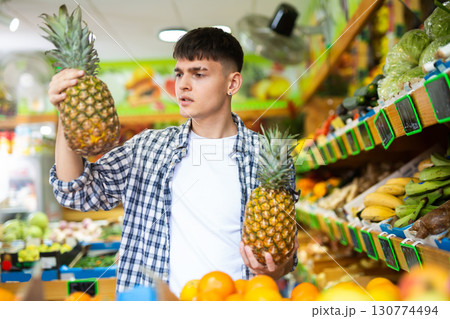 Young European male shopping and choosing pineapples at supermarket 130774494