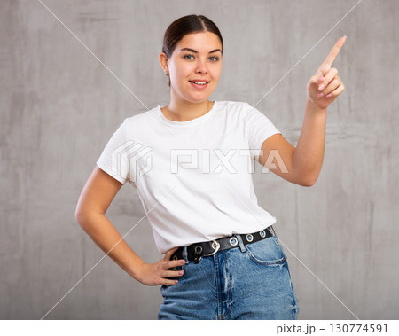 Cheery young woman pointing fingers away against gray background Cheery young woman pointing fingers away against gray background 130774591