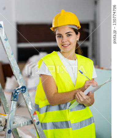 Positive female civil engineer taking notes while checking construction site Positive female civil engineer taking notes while checking construction site 130774706