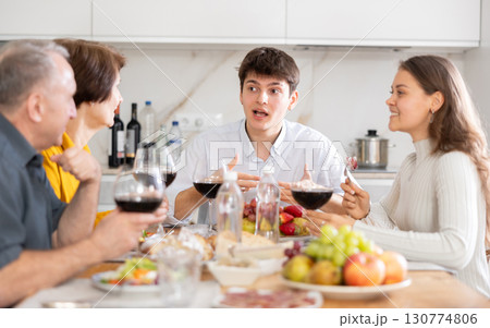 Smiling young man talking with family at festive table with wine and snacks at home Smiling young man talking with family at festive table with wine and snacks at home 130774806