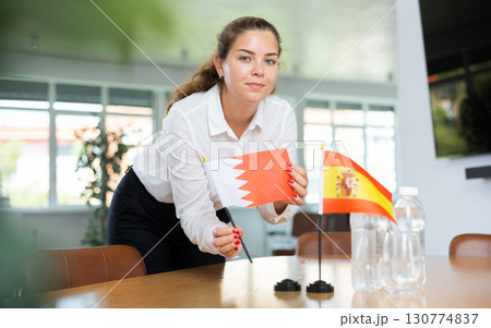 Young woman putting Bahrain and Spain flags on table in office 130774837