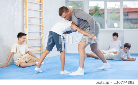 Skilled trainer demonstrating self-defense technique on juvenile practitioner 130774892