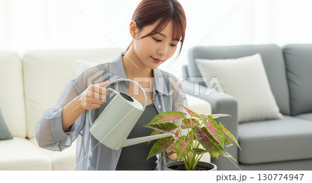 リビングに置かれた植物に水をやる女性 130774947