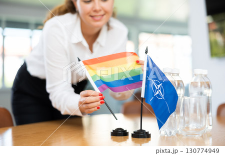 Preparing for business negotiations - woman sets small flags of countries of NATO (OTAN) and LGBT on table Preparing for business negotiations - woman sets small flags of countries of NATO (OTAN) and LGBT on table 130774949