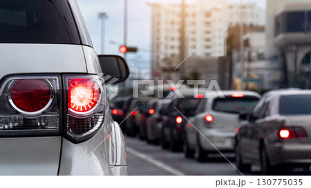 Rear side of white luxury car with turn on brake light. Traffic jam in the city with car lights and traffic jam. background of tall building. 130775035