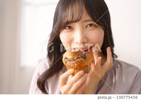美味しそうにマフィンを食べる若い女性 美味しそうにマフィンを食べる若い女性 130775438