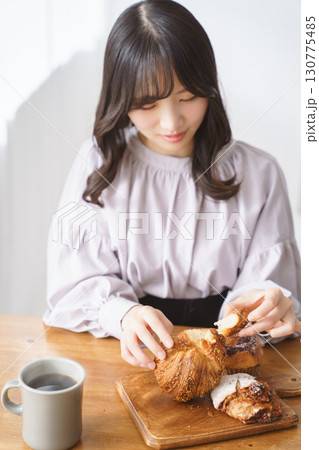 小さく千切ってパンを食べる若い女性 130775485