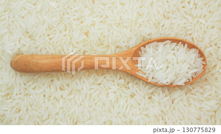 Raw white rice grains on wooden spoon laying flat on heap of rice background. Perfect for illustrating Asian cuisine, Thai rice Raw white rice grains on wooden spoon laying flat on heap of rice background. Perfect for illustrating Asian cuisine, Thai rice 130775829
