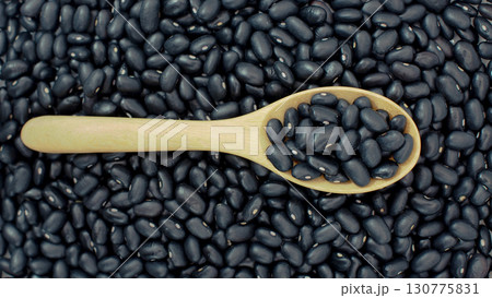 Raw black beans on horizontal wooden spoon over heap of black beans background. Ideal for illustrating legumes, organic agriculture 130775831