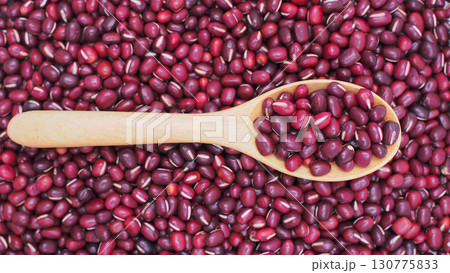 Raw red adzuki beans on horizontal wooden spoon over heap of red beans background. Ideal for illustrating legumes, organic food Raw red adzuki beans on horizontal wooden spoon over heap of red beans background. Ideal for illustrating legumes, organic food 130775833