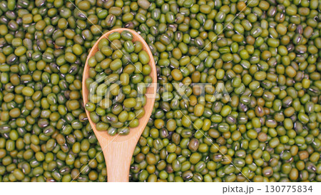 Raw green mung beans on wooden spoon over heap of mung beans background. Perfect for illustrating legumes, natural food ingredients Raw green mung beans on wooden spoon over heap of mung beans background. Perfect for illustrating legumes, natural food ingredients 130775834
