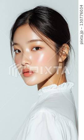 Young Korean woman with radiant skin poses gracefully against a light background during a photo shoot in a stylish outfit 130776034