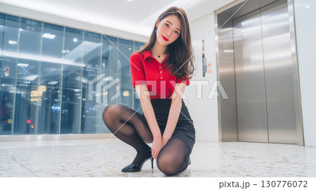 Young woman in a stylish outfit poses confidently indoors near an elevator in a modern building during the evening 130776072
