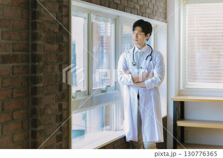 窓辺に立つ白衣を着た若い医師 窓辺に立つ白衣を着た若い医師 130776365