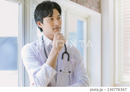 窓辺に立つ白衣を着た若い医師 130776367