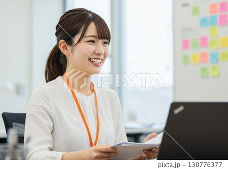 オフィスで笑顔の女性社員｜書類・パソコン業務・ビジネスシーンに活用できるフリー素材写真 130776377