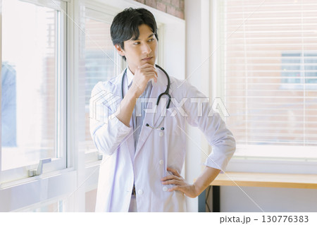窓辺に立つ白衣を着た若い医師 130776383