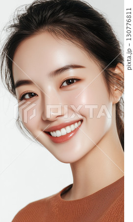 Beautiful Korean woman with a radiant smile posing against a plain background, showcasing natural beauty and healthy skin Beautiful Korean woman with a radiant smile posing against a plain background, showcasing natural beauty and healthy skin 130776811