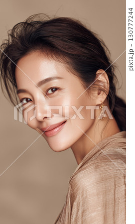 Beautiful Korean woman with glowing skin smiles softly against a neutral backdrop in a fashion-forward portrait 130777244