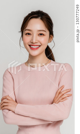 Smiling Korean woman poses confidently with crossed arms, showcasing her beauty and warmth in a bright and inviting atmosphere Smiling Korean woman poses confidently with crossed arms, showcasing her beauty and warmth in a bright and inviting atmosphere 130777249
