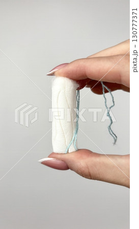 Female hand holding white tampon on clean white background, close up. Feminine hygiene product for menstruation, womens health and period care concept 130777371