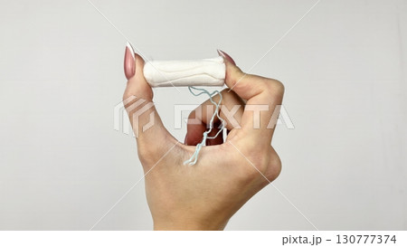 Female hand holding white tampon on clean white background, close up. Feminine hygiene product for menstruation, womens health and period care concept 130777374