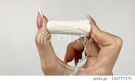 Female hand holding white tampon on clean white background, close up. Feminine hygiene product for menstruation, womens health and period care concept 130777375
