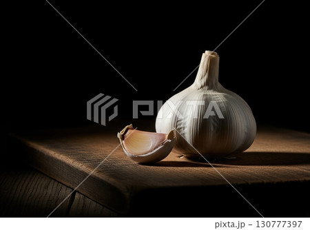 Fresh garlic bulb with a single clove on a rustic wooden board against a black background 130777397
