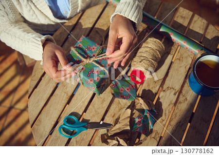Person Wrapping a Gift with Decorative Paper on Wooden Table Outdoors 130778162