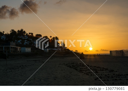 砂浜の海岸の先の建物が並ぶ丘の脇から昇る夜明けの太陽 スペインのフエルテベンテュラ島にて 砂浜の海岸の先の建物が並ぶ丘の脇から昇る夜明けの太陽 スペインのフエルテベンテュラ島にて 130779081