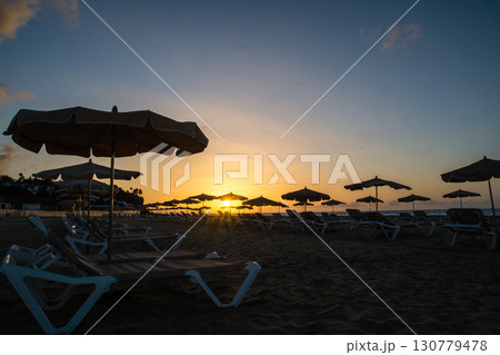 水平線から昇るまぶしい朝日と海岸線の砂浜に並べられたビーチベッドとパラソル　フエルテベンテュラ島にて 130779478