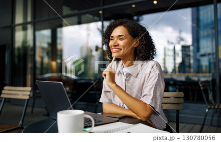 A joyful and smiling woman is working diligently on her laptop in a modern and trendy cafe setting A joyful and smiling woman is working diligently on her laptop in a modern and trendy cafe setting 130780056
