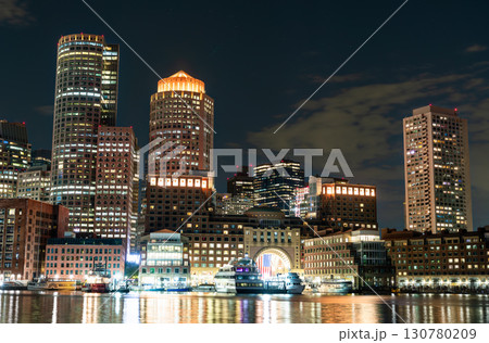 The illuminated downtown Boston skyline, including the Boston Harbor Hotel with its iconic arch, reflecting on the water of the harbor at night. Massachusetts, United States 130780209